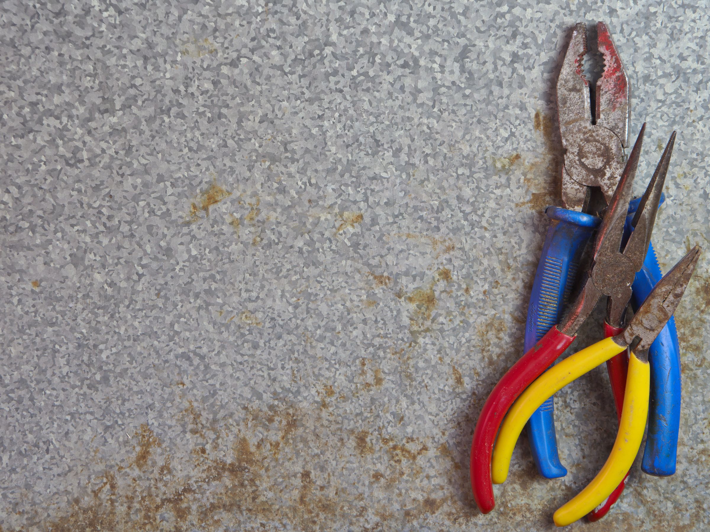 Three pairs of pliers on a galvanized metal surface
